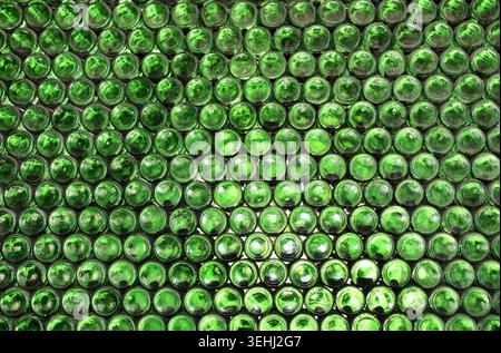 Full frame wall with empty green beer bottles bottoms. Alcohol theme. Endless rows of wine bottles. Green glass bottle wall with sunlight from behind Stock Photo