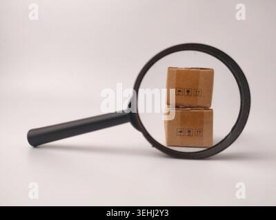 A magnifying glass focuses on a stack of two miniature brown cardboard boxes with fragile symbols. Stock Photo