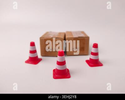 Three small red and white plastic traffic cones surround two miniature cardboard boxes in the center. Stock Photo