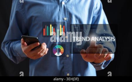 Man interacting with a virtual screen displaying trend analysis, data charts, and innovation concepts, holding a smartphone Stock Photo