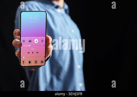 Hand holding modern smartphone displaying a music player and quick settings user interface on screen. Technology and connectivity concept Stock Photo