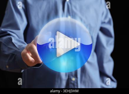 Man's hand interacting with a shimmering blue play icon, symbolizing digital media, streaming, and future technology Stock Photo