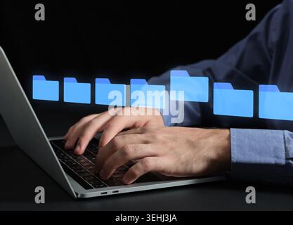 Person's hands typing on a laptop with holographic folder icons representing digital data or digital asset management and cloud storage Stock Photo