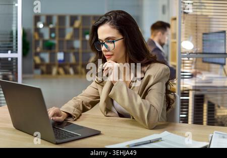 Focused businesswoman manager using laptop working at modern office desk indoors Stock Photo