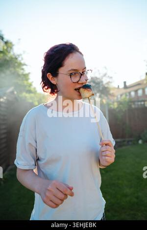 Young woman eating toasted marshmallow in sunny backyard garden Stock Photo