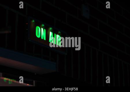 Illuminated green neon sign with text On Air hanging in a dark broadcasting or recording studio. Technical equipment backdrop for podcasting, radio st Stock Photo