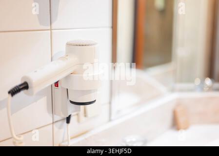 Wall-mounted white hotel hairdryer in a bright modern bathroom, close-up. Stock Photo