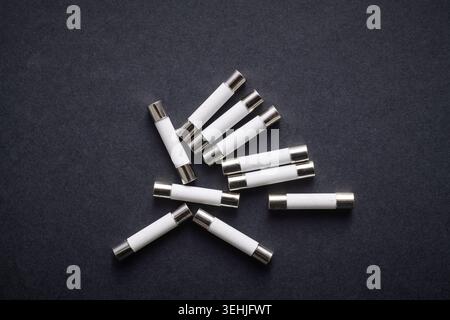 Set of miniature electrical ceramic tube fuses for overcurrent protection in electrical circuits on a black table Stock Photo