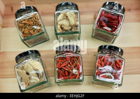 Beautiful inviting rustic glass jar collection containing dried spice chili pepper herb ingredient resting on warm wooden background for culinary cook Stock Photo