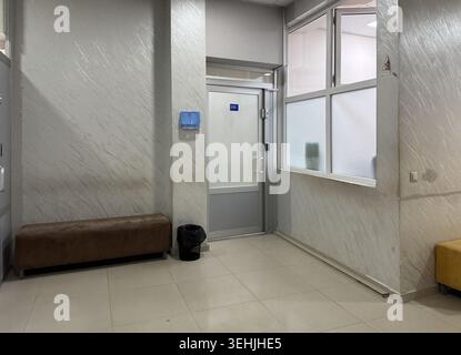 A waiting area shows a brown bench along the wall, a trash can beside it, and two doors leading to different rooms. Natural light comes through window Stock Photo