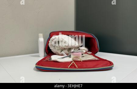 Tools and items in a red bag on a white table with various grooming and personal care products inside Stock Photo