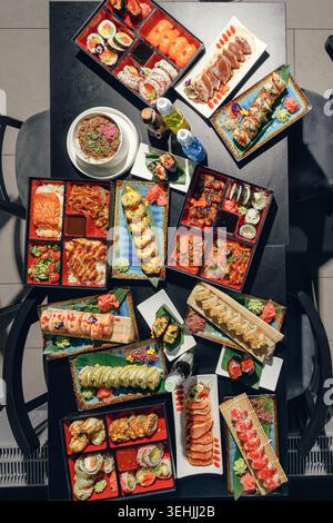 Table in an Asian restaurant with dishes. Sushi, poke bowls, soups, bento box. Studio light. Film effect Stock Photo