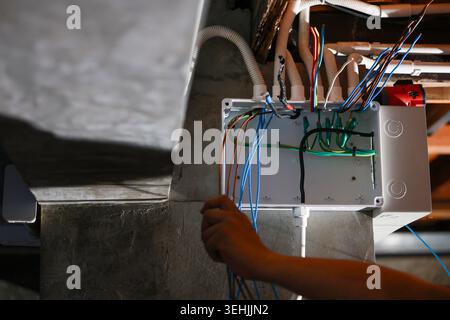 Focused electrician doing electrical wire box junction installation by hand during repair and construction work in dark industrial basement setting wi Stock Photo