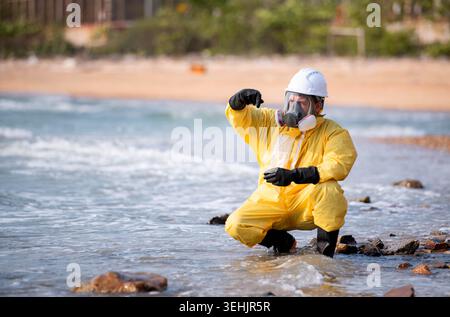 Scientists in yellow suits are collecting water samples from the coastline, flowing away from an oil refinery, before taking the water to the laboratory for further analysis Stock Photo
