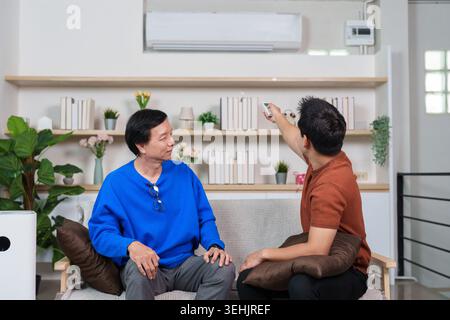 Asian young man adjusting smart home air conditioner for senior Stock Photo