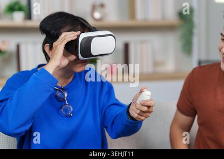 Asian senior man experiencing virtual reality gaming with young man at home Stock Photo