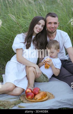 Parents And Kid Enjoying Sunny Day. Parents And Child Sitting On Blanket Among Lush Grassy Field Stock Photo