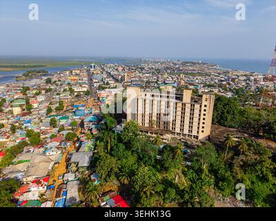 Aerial view of a large multi-story building on a lush green hill overlooking the dense urban sprawl and coastline of Monrovia, Liberia. Stock Photo