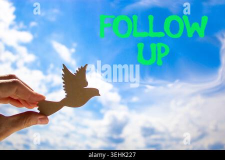 Follow up symbol. Concept word Follow up on beautiful blue sky. Businessman's hand with wooden bird. Beautiful blue sky and cloud background. Business Stock Photo