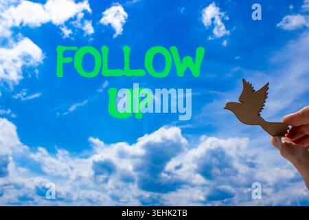 Follow up symbol. Concept word Follow up on beautiful blue sky. Businessman's hand with wooden bird. Beautiful blue sky and cloud background. Business Stock Photo