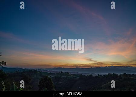 A breathtaking sunset over layered mountain ranges, with warm golden light fading into a deep blue sky, creating a serene and expansive natural landsc Stock Photo