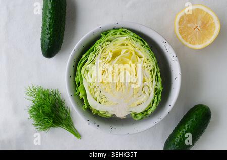 Fresh vegetables and herbs with halved lemon, cabbage, cucumbers, and dill on light fabric background. Healthy eating, organic farming, and natural in Stock Photo