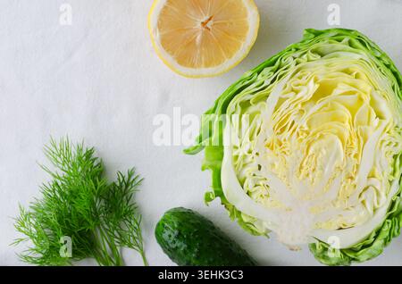 Fresh vegetables and herbs with halved lemon, cabbage, cucumbers, and dill on light fabric background. Healthy eating, organic farming, and natural in Stock Photo