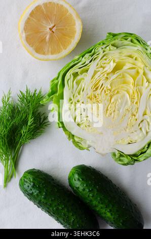 Fresh vegetables and herbs with halved lemon, cabbage, cucumbers, and dill on light fabric background. Healthy eating, organic farming, and natural in Stock Photo