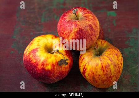 Three apples (Malus domestica) with red and yellow skin are stacked on a dark, textured surface. Stock Photo