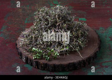 A pile of dried and fresh thyme (Thymus vulgaris) rests on a circular wooden slice. Stock Photo