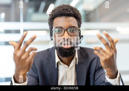 Confident customer service agent wearing a headset and glasses, communicating with clients, providing support, discussing solutions, and offering professional assistance in an office environment Stock Photo