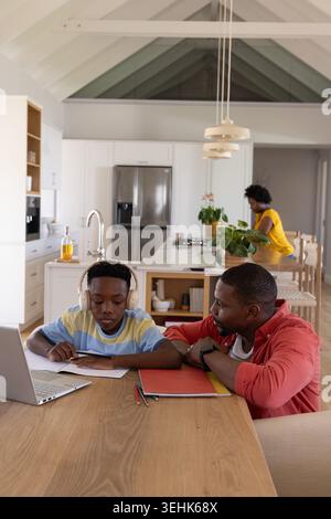 African American family father in red shirt helping child with headset using laptop at dining table Stock Photo