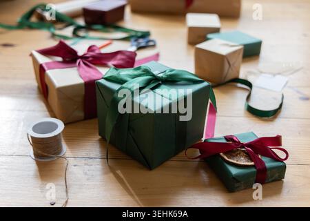 Dark green square gift box sitting centered on wooden tabletop, kraft gifts and twine surrounding Stock Photo