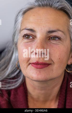 Senior woman posing in studio, wearing burgundy knit, gold hoops and mauve lipstick, looking upward Stock Photo