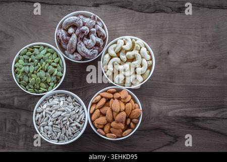 Nuts of different varieties lie in bowls on a wooden table, top view. Assortment of nuts and pumpkin seeds, sunflower seeds, cashews and almonds nuts Stock Photo