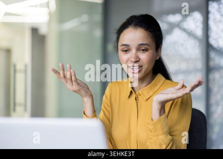 Businesswoman leading a virtual meeting from her office, engaging on laptop with expressive hand gestures while discussing projects and collaborating remotely with colleagues online Stock Photo