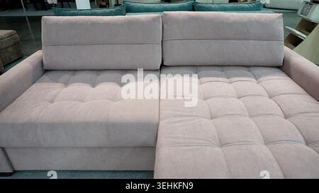Close up of contemporary L-shaped sofa with soft, tufted fabric upholstery. Neutral pastel pink color furniture for sale in showroom. Modern interior Stock Photo