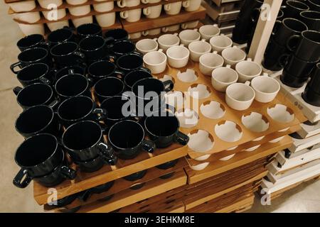 Black and white ceramic cups arranged on shelves in a modern home goods store. Minimal kitchenware concept for cafe and interior lifestyle themes. Stock Photo