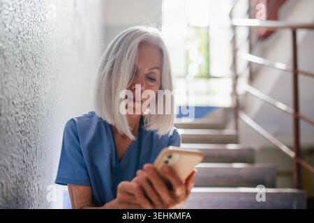Tired nurse taking break during hospital shift, texting with family. Stock Photo