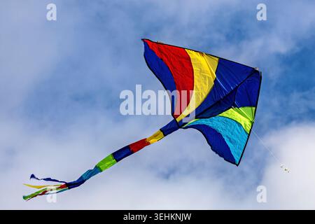 A colourful kite soars against the cloudy blue sky in the wind Stock Photo