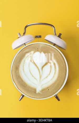 Food, It's coffee time, the signal to drink your morning cappuccino or latte. Concept with a cup of coffee on the display of a vintage alarm clock Stock Photo