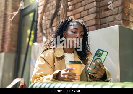 Pensive african american woman scrolling media on smartphone online while resting in cafe outdoors. Stock Photo