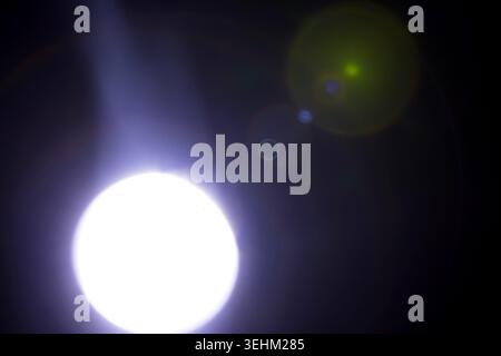 Bright circular light source with beams and lens flares against a dark background, showcasing varying light intensity and color effects Stock Photo