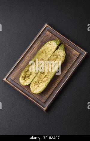 Food, Delicious zucchini cut into two halves baked with salt, spices and herbs on a dark concrete background Stock Photo