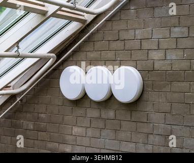 A series of modern, round bulkhead light fixtures mounted on an industrial brick wall. Stock Photo