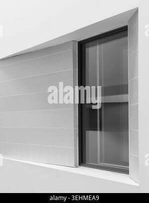 Close-up monochrome detail of a contemporary building facade showing a ribbed render panel beside a recessed glazed window. Stock Photo