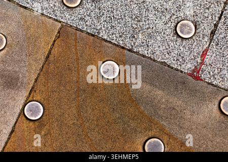 Abstract close-up of patterned stone paving slabs with metal stud fixings, contrasting textures and tones. Stock Photo