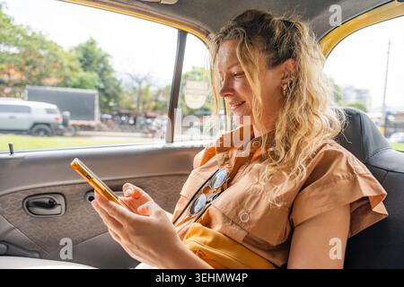 A solo traveler explores Medellin, Colombia, enjoying a sunny taxi ride while using her phone. A glimpse of urban tourism and modern exploration in a Stock Photo