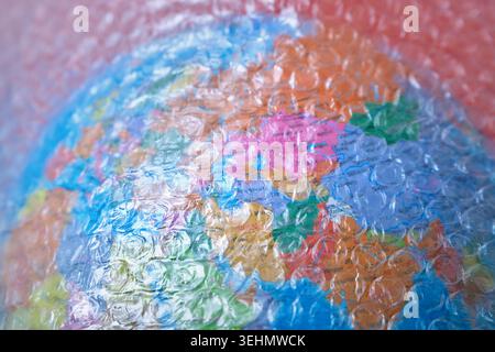 Close-up of a colorful world globe covered with clear bubble pack wrapping plastic, creating a textured abstract background that suggests shipping, pr Stock Photo