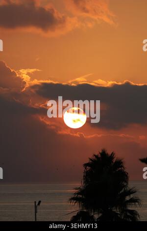 A stunning sunset view with the glowing sun partially hidden behind dark clouds. The sky transitions from deep orange to subtle pink, casting unique s Stock Photo